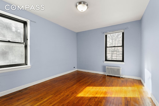 spare room featuring radiator heating unit, wood-type flooring, and baseboards