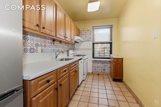 kitchen with freestanding refrigerator, light tile patterned floors, white gas stove, under cabinet range hood, and a sink