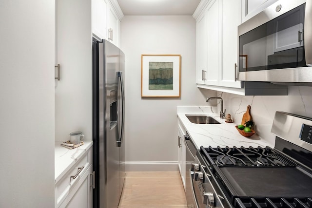 kitchen with stainless steel appliances, white cabinets, a sink, and light stone counters