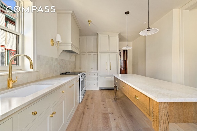 kitchen with stainless steel range with electric cooktop, a sink, decorative light fixtures, and white cabinetry