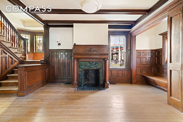 unfurnished living room with a high end fireplace, stairs, light wood-type flooring, beam ceiling, and ornate columns