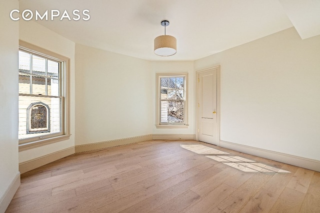 spare room featuring a healthy amount of sunlight, light wood-type flooring, and baseboards