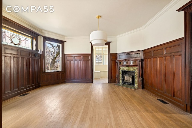 unfurnished living room featuring light wood finished floors, a fireplace, ornamental molding, and a wainscoted wall