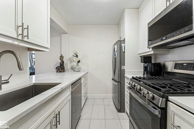 kitchen with light stone counters, appliances with stainless steel finishes, a sink, and white cabinetry