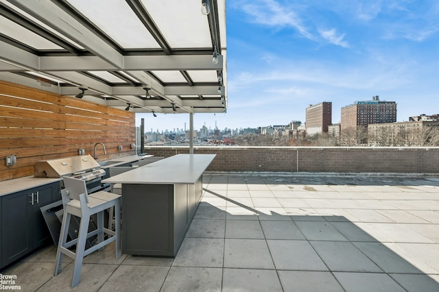 view of patio featuring outdoor wet bar, exterior kitchen, area for grilling, a fenced backyard, and a city view