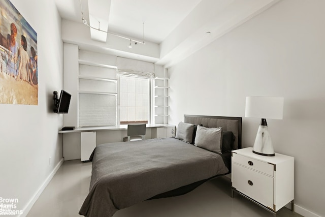 bedroom with rail lighting, concrete floors, built in desk, and baseboards