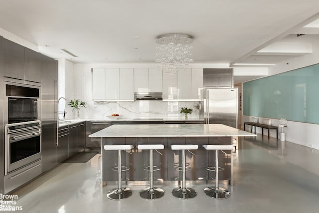 kitchen featuring a breakfast bar area, stainless steel appliances, a kitchen island, white cabinetry, and modern cabinets