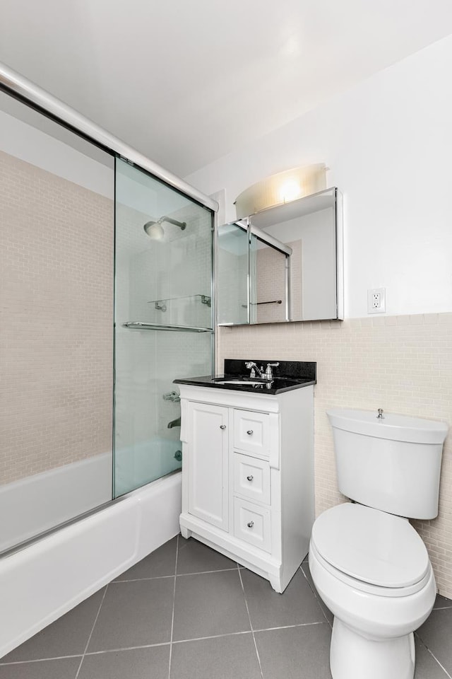 bathroom with tile walls, toilet, enclosed tub / shower combo, vanity, and tile patterned flooring