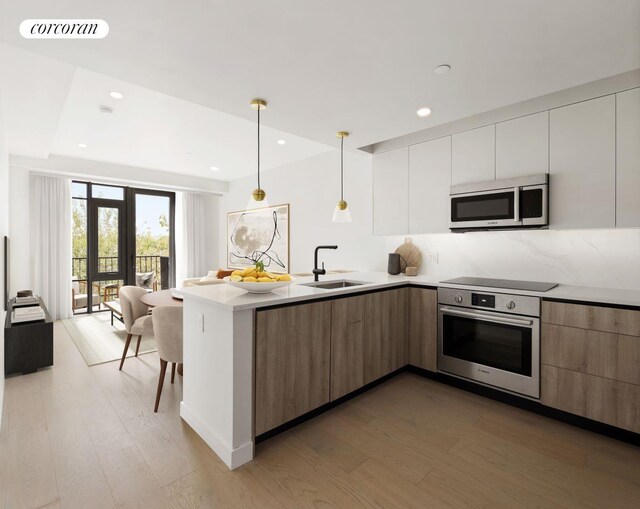 kitchen with a peninsula, a sink, appliances with stainless steel finishes, light wood-type flooring, and modern cabinets