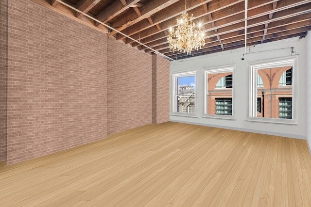 empty room with a notable chandelier, brick wall, and wood finished floors