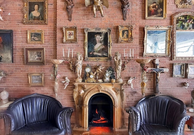 sitting room featuring a warm lit fireplace and brick wall