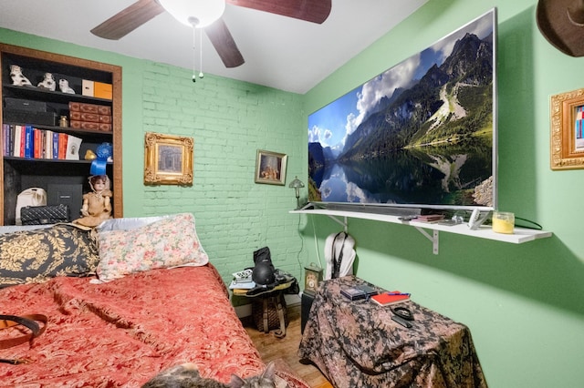 interior space with a ceiling fan, brick wall, and wood finished floors