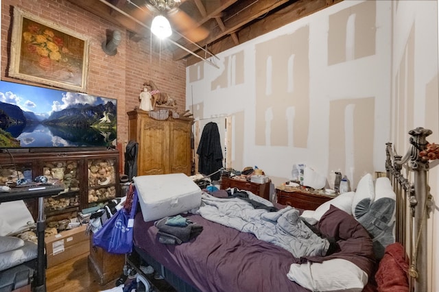 bedroom featuring brick wall, a high ceiling, and wood finished floors