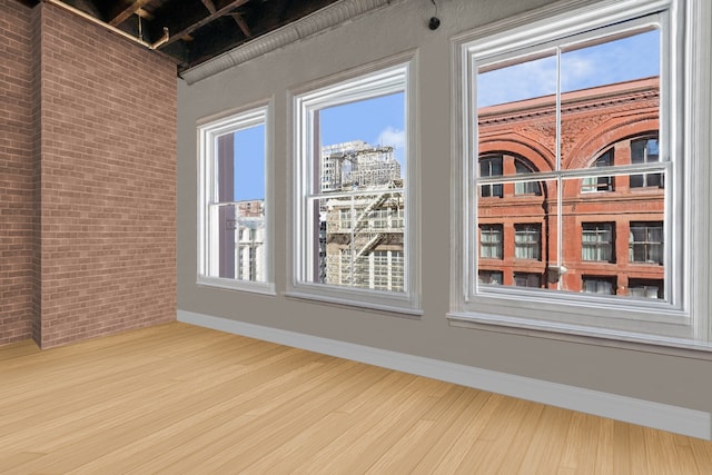 empty room featuring brick wall, wood finished floors, a city view, and baseboards