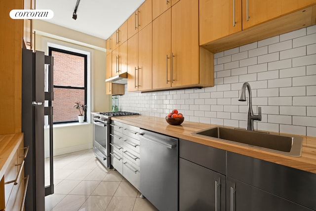 kitchen featuring light tile patterned floors, tasteful backsplash, stainless steel appliances, wooden counters, and a sink