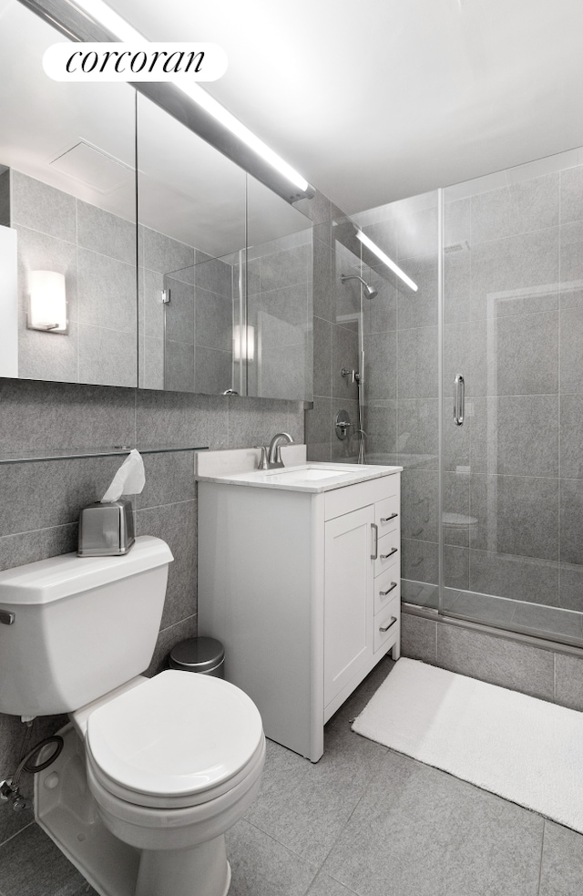 full bathroom with tile walls, toilet, a shower stall, vanity, and tile patterned floors