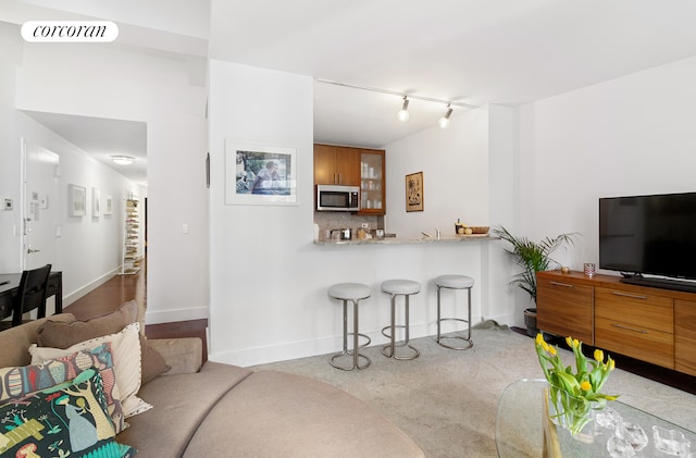 kitchen featuring a breakfast bar, brown cabinets, tasteful backsplash, stainless steel microwave, and visible vents