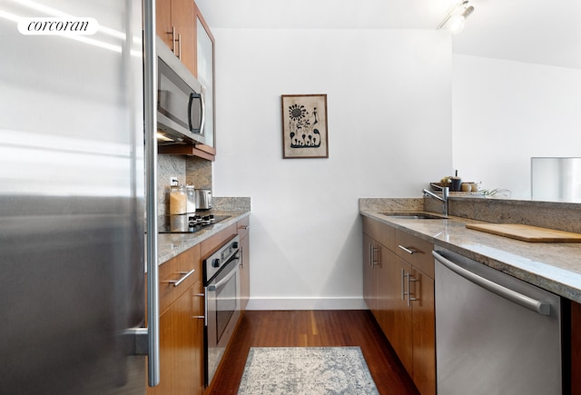 kitchen featuring decorative backsplash, dark wood-style floors, appliances with stainless steel finishes, brown cabinets, and a sink