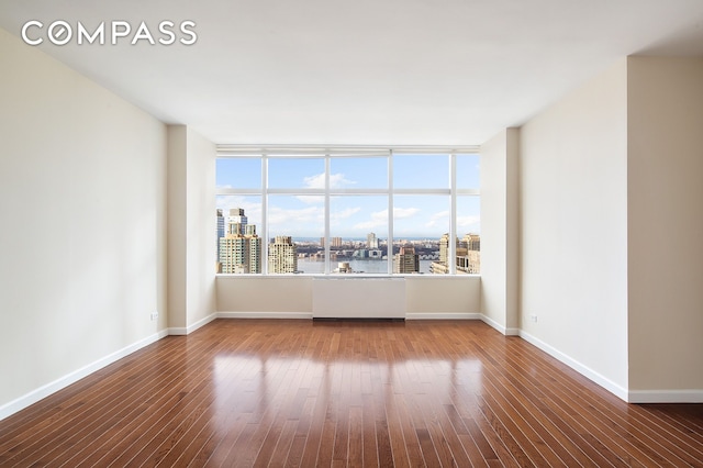 unfurnished room featuring a view of city, wood finished floors, and baseboards