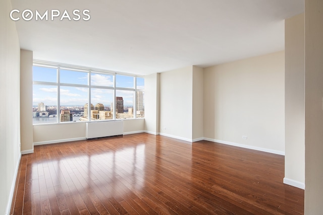 spare room featuring baseboards, dark wood finished floors, and a city view