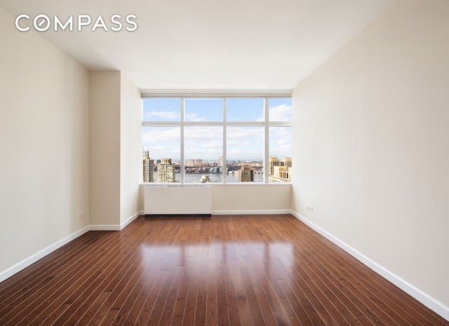 unfurnished room with a view of city, baseboards, and wood finished floors