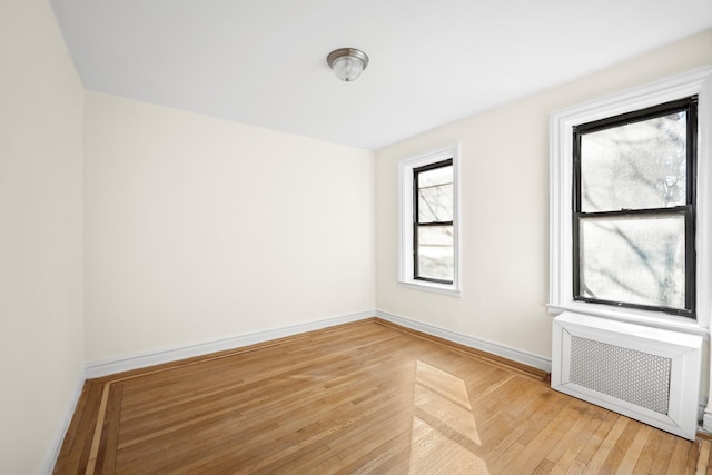 empty room with light wood finished floors, radiator heating unit, and baseboards