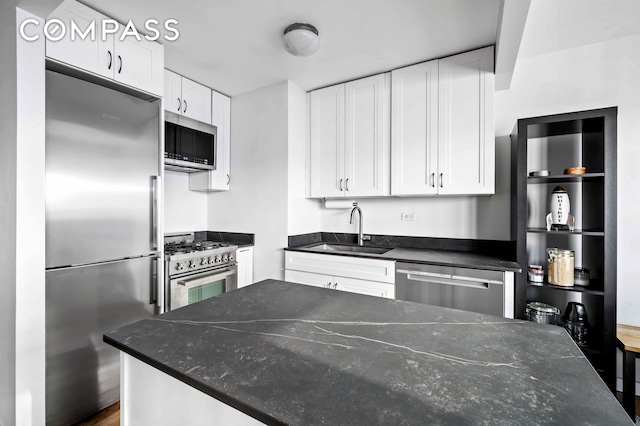 kitchen featuring dark stone countertops, white cabinets, high end appliances, and a sink