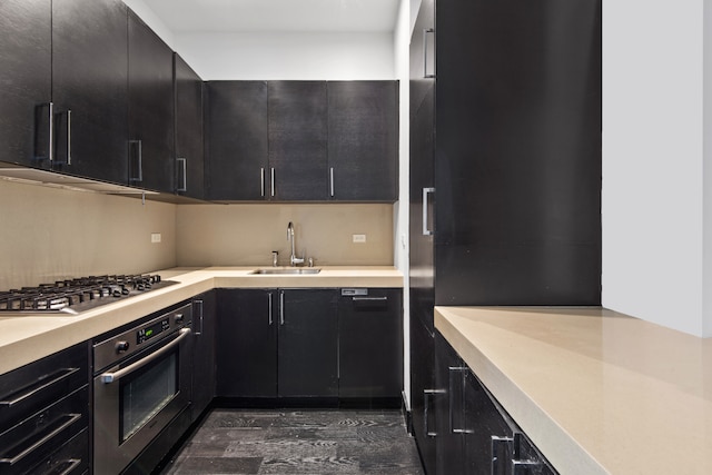 kitchen featuring light countertops, appliances with stainless steel finishes, a sink, and dark cabinetry