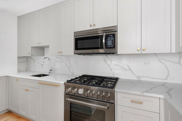 kitchen featuring white cabinets, appliances with stainless steel finishes, light stone counters, and a sink