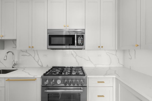 kitchen with light stone countertops, stainless steel appliances, a sink, white cabinetry, and decorative backsplash