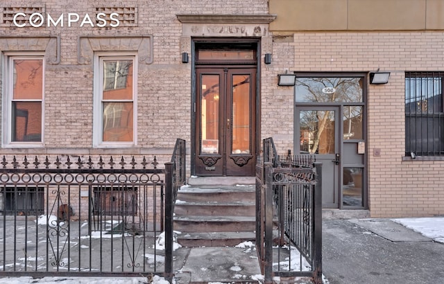 snow covered property entrance featuring fence and brick siding