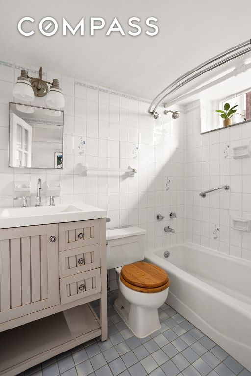 full bath featuring tile patterned flooring, toilet, shower / bath combination, vanity, and tile walls