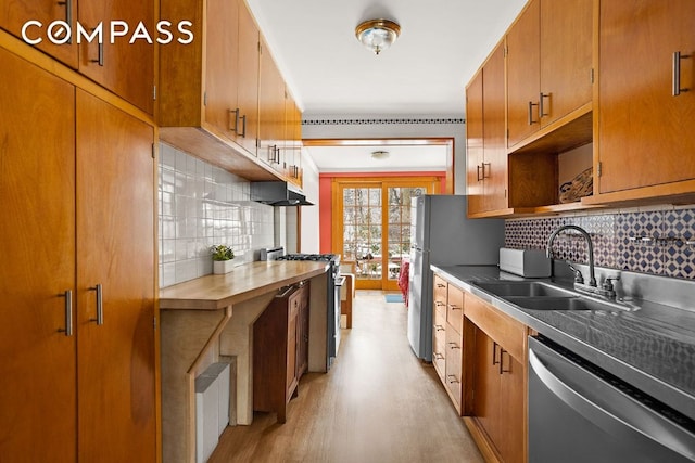 kitchen featuring under cabinet range hood, a sink, appliances with stainless steel finishes, brown cabinets, and decorative backsplash