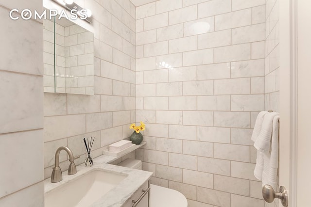 half bath with tile walls, vanity, and toilet