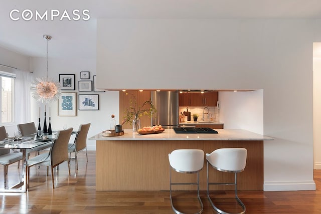 kitchen featuring decorative backsplash, wood finished floors, freestanding refrigerator, a peninsula, and a sink