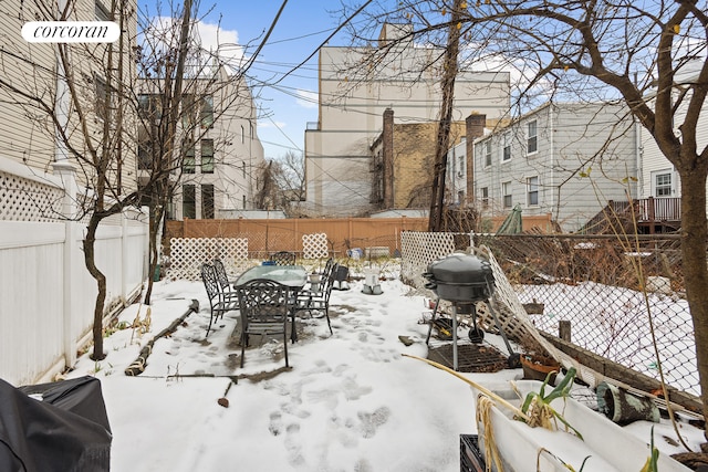 snow covered patio with outdoor dining space, a fenced backyard, and grilling area