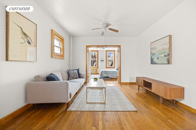 living room featuring a ceiling fan, visible vents, baseboards, and wood finished floors