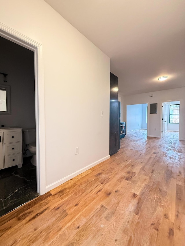 empty room featuring electric panel, baseboards, and light wood finished floors