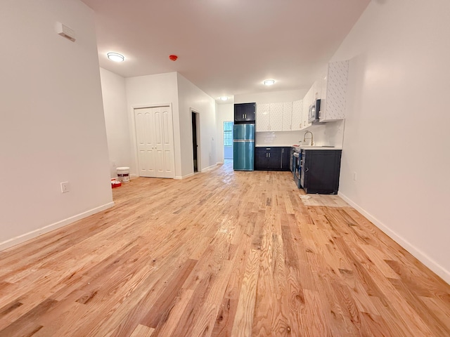 unfurnished living room with a sink, baseboards, and light wood-style floors