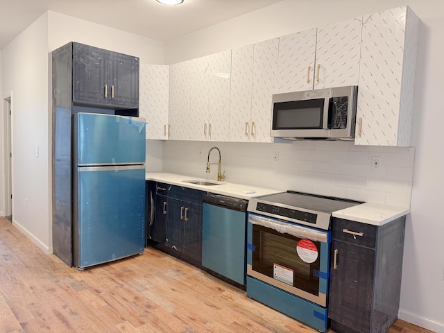 kitchen featuring light wood-style flooring, a sink, backsplash, appliances with stainless steel finishes, and light countertops