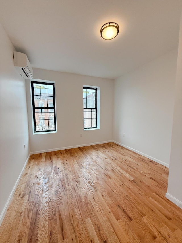 empty room with light wood-type flooring, a wall mounted AC, and baseboards