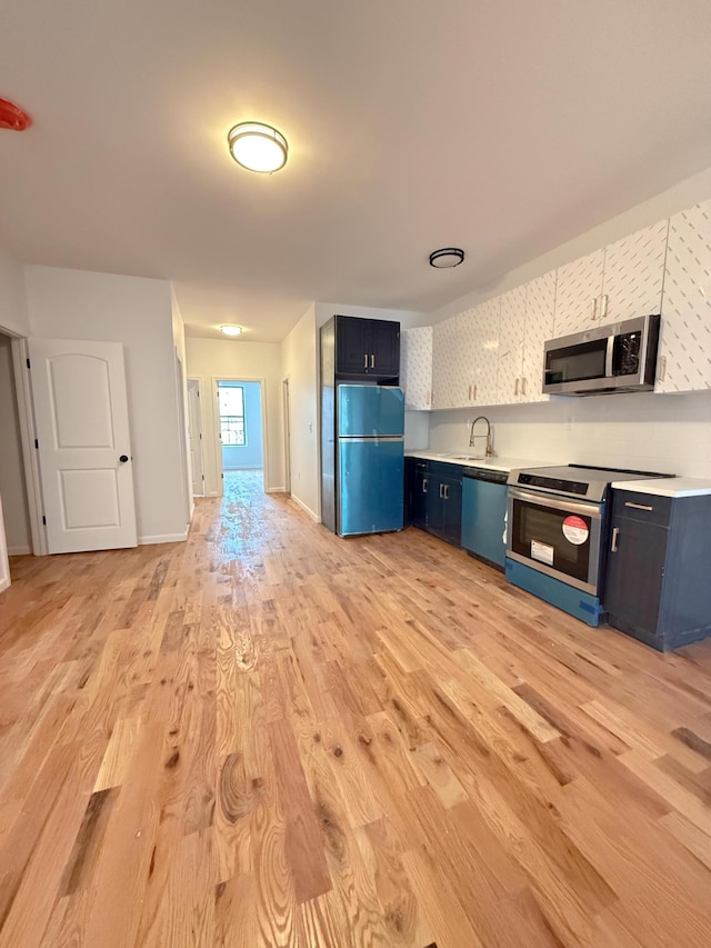 kitchen with blue cabinets, light wood-style flooring, a sink, appliances with stainless steel finishes, and light countertops