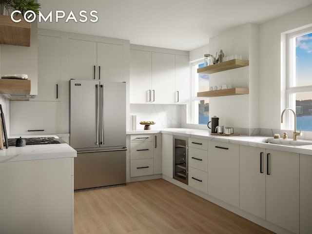 kitchen with light stone countertops, open shelves, high end fridge, a sink, and light wood-style floors