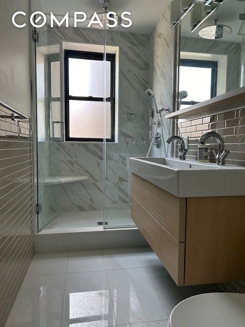 bathroom with a marble finish shower, tile walls, toilet, tile patterned floors, and vanity