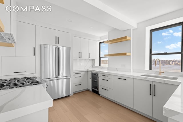 kitchen featuring high end fridge, light stone counters, open shelves, a sink, and wine cooler