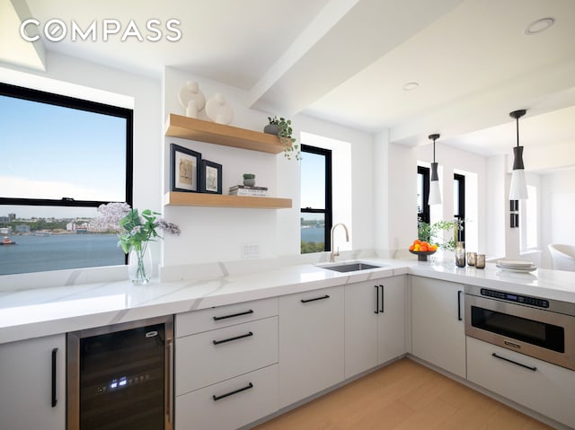 kitchen featuring oven, beverage cooler, white cabinets, a sink, and light wood finished floors