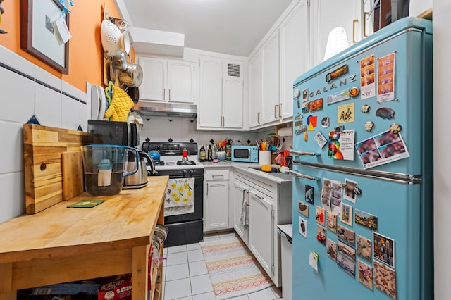 kitchen with freestanding refrigerator, gas stove, white microwave, under cabinet range hood, and white cabinetry