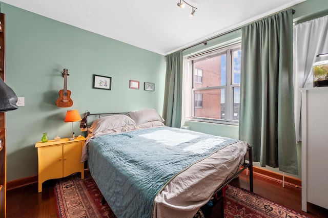 bedroom featuring track lighting, dark wood-style flooring, and baseboards