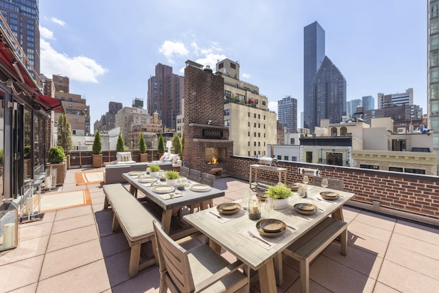 view of patio / terrace with an outdoor brick fireplace, outdoor dining space, and a city view