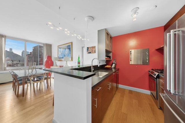 kitchen featuring stainless steel appliances, a sink, dark countertops, modern cabinets, and light wood-type flooring